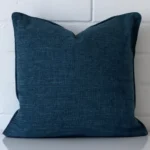 A linen square cushion cover that has a unique design is shown vertically against a brick wall. It has a wonderful cobalt blue colour.