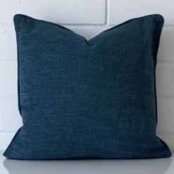 A linen square cushion cover that has a unique design is shown vertically against a brick wall. It has a wonderful cobalt blue colour.