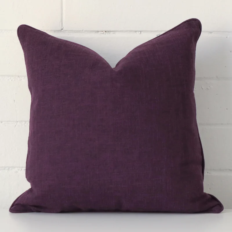 albon-plum-cushion-cover-45m-x-45cm-sc792-45 A square cushion in a delightful plum tone rests against a white wall. The linen material appears to be of exceptional quality.