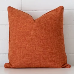 A brick wall that has a rust cushion cover positioned in front of it. It has an exquisite linen material and a lovely square shape.