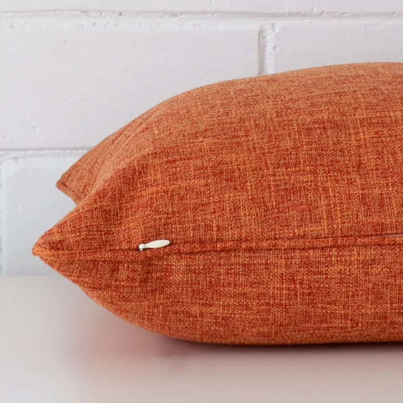 Horizontal edge view of front and back panels of a linen cushion in a square size and with rust colouring.