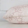 A floral light pink cushion cover is laid flat. This angle shows the side of the linen fabric and its rectangle shape.