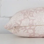 A floral light pink cushion cover is laid flat. This angle shows the side of the linen fabric and its rectangle shape.