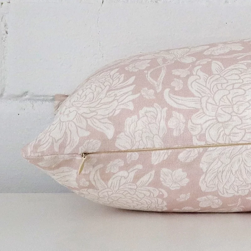 A floral light pink cushion cover is laid flat. This angle shows the side of the linen fabric and its rectangle shape.
