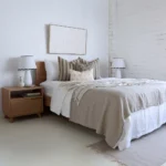 A bright white bedroom with 4 designer cushions sitting on a wooden bed.