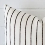 Horizontal edge of striped square cushion cover is shown. The linen fabric can be seen up close from this side view.