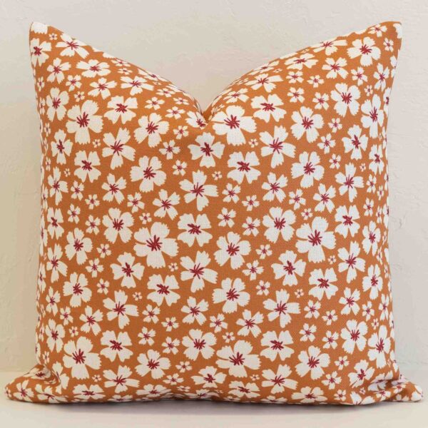 Amora ditsy floral cushion with white flowers on warm orange background.
