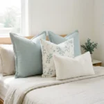 Set of four cushions with sage linen, a botanical print, and a white boucle lumbar, on a bed.