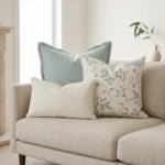 Trio of cushions with sage linen, a botanical print, and a white boucle lumbar, on a couch.