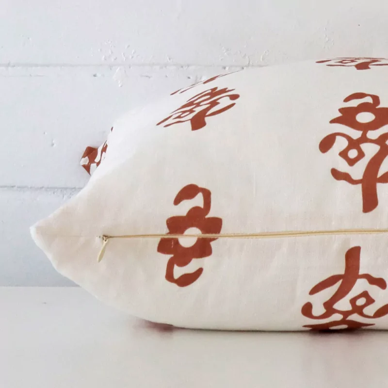 A square linen cushion positioned flat to show its seams. The terracotta colour and design are visible as is the seam between the panels.