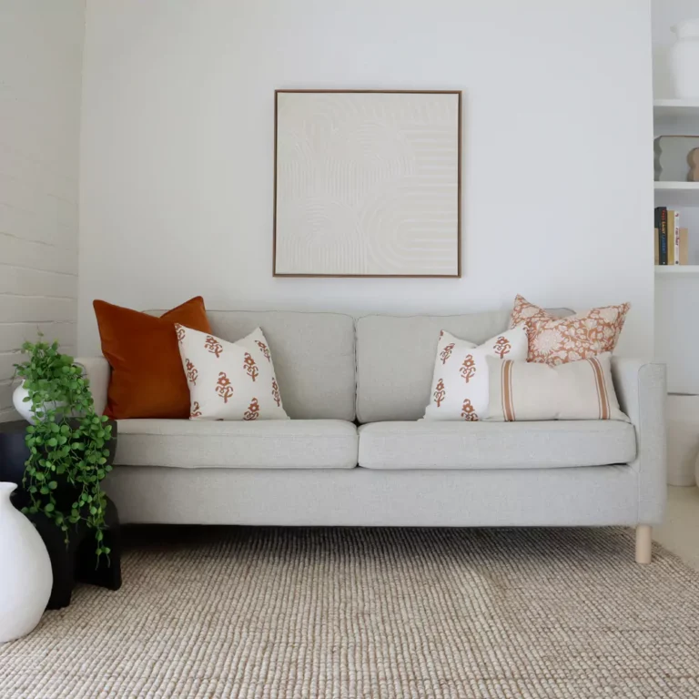 Seven terracotta sofa cushions on a sofa next to a white brick wall.