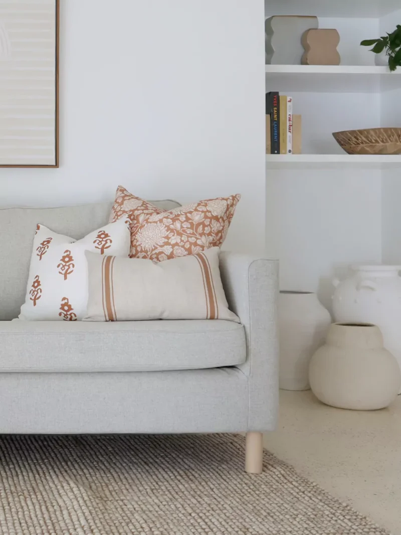 Terracotta-coloured cushions from the Aria sofa cushion set are displayed on a corner of a grey sofa.