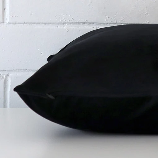 A large black cushion cover laying flat. This viewpoint highlights the velvet fabric from a side position.
