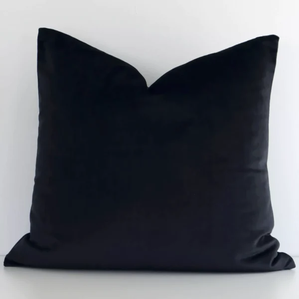 A lovely square black cushion cover arranged in front of a white wall. The solid colour style complements the velvet material.