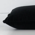 A black cushion arranged sideways in front of a wall. The rectangle size and velvet fabric are shown and the seams are clearly visible.