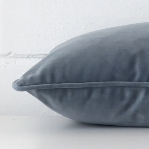 A rectangle blue grey cushion cover laying flat. This viewpoint highlights the style and velvet fabric from a side position.