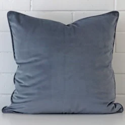 Here a blue grey velvet cushion is shown styled against a white wall. It has a large size.