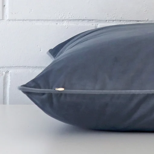 A blue grey cushion positioned on its back panel. The shot shows a lateral view of the velvet fabric and its size.
