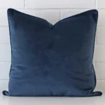 A velvet large cushion cover is shown vertically against a brick wall. It has a wonderful blue colour.
