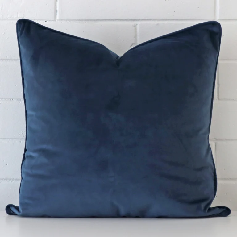 A velvet large cushion cover is shown vertically against a brick wall. It has a wonderful blue colour.