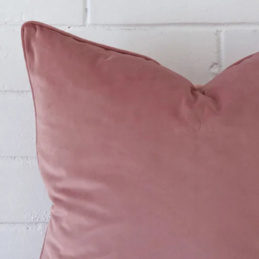 A very close image of the corner of a velvet cushion.The finer detail of the large shape and blush colour are visible.