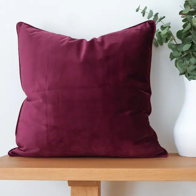 A bold velvet cushion is styled on wooden seating with foliage at edge of shot.