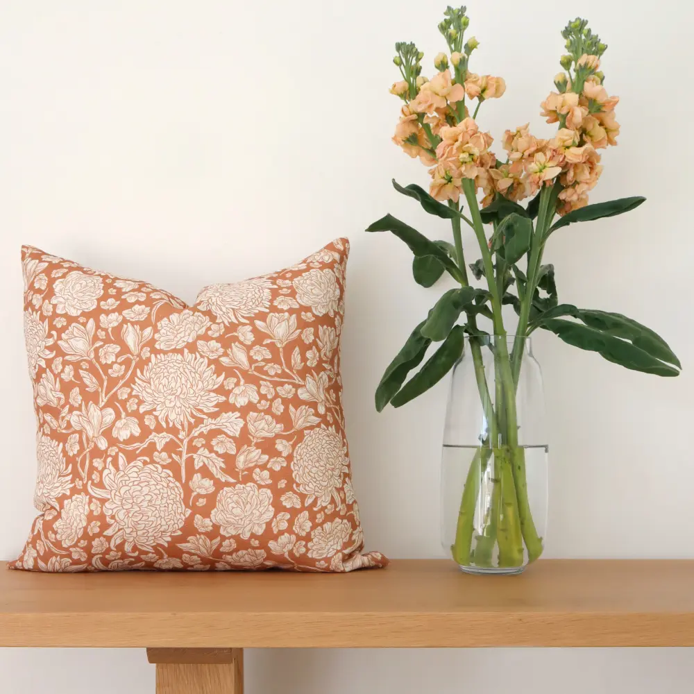 A bunch of flowers sits on a wooden seat next to some floral cushions.