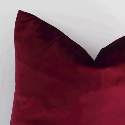 Close up of a burgundy cushion in burgundy. The quality of its solid colour design is shown in fine detail.