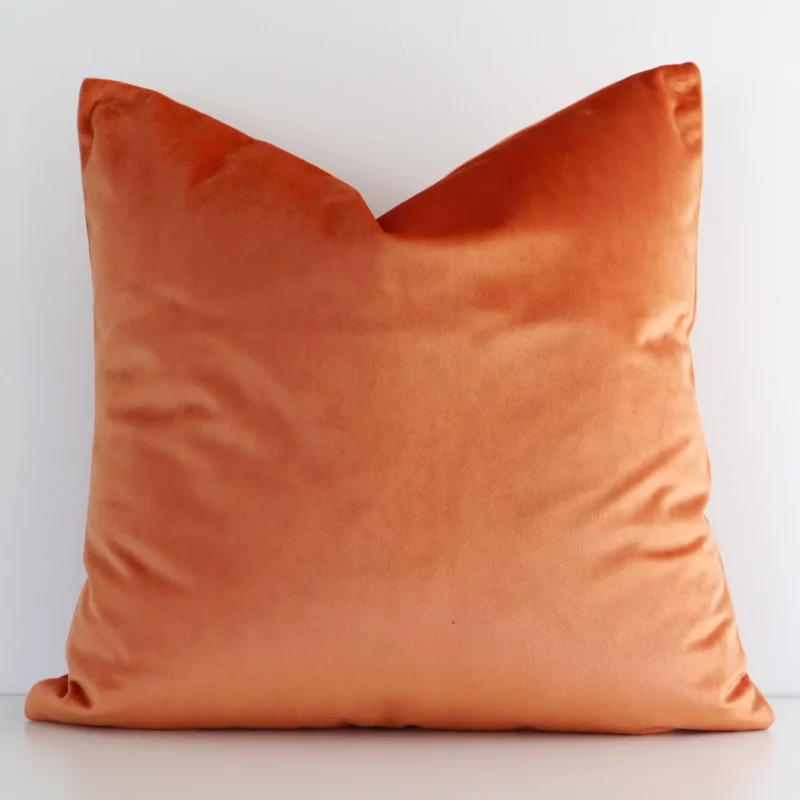 burnt-orange-velvet-linen-cushion-cover---sc515-45 A square solid colour cushion in a delightful burnt orange tone rests against a white wall. The velvet material appears to be of exceptional quality.