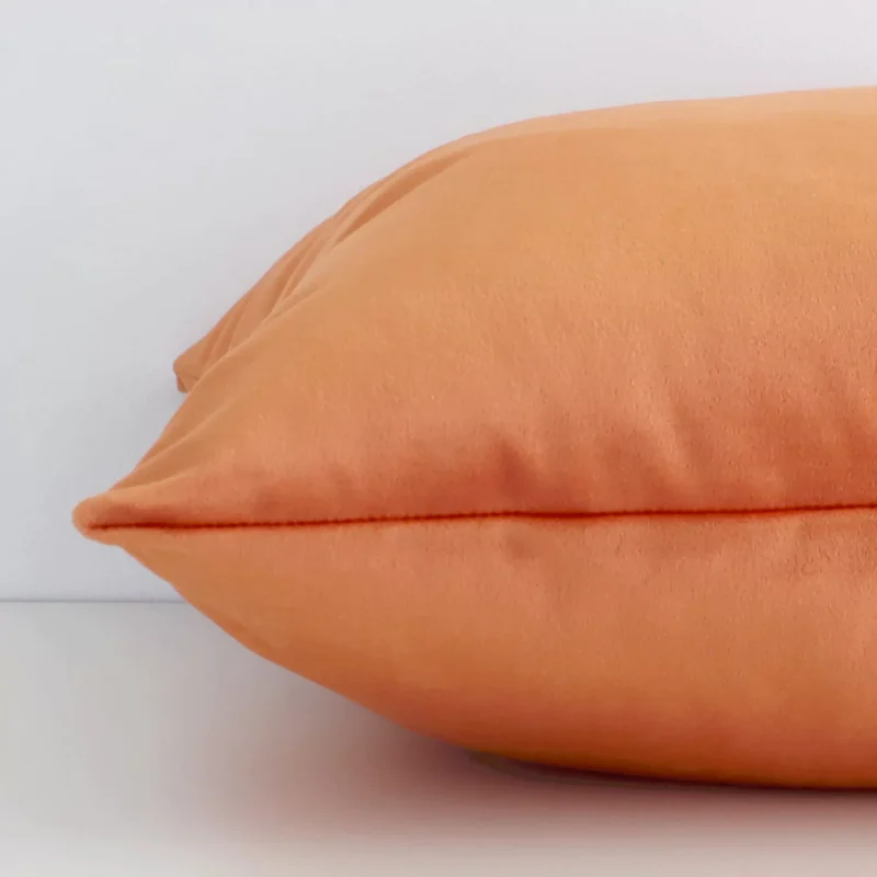 A velvet burnt orange cushion cover shown laying on its side. The solid colour design and its square size are shown side on.