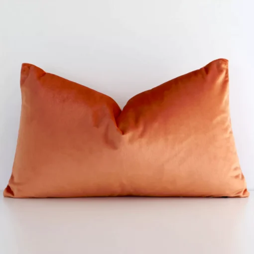 A velvet rectangle cushion cover that has a lovely solid colour design is shown vertically against a white wall. It has a wonderful burnt orange colour.