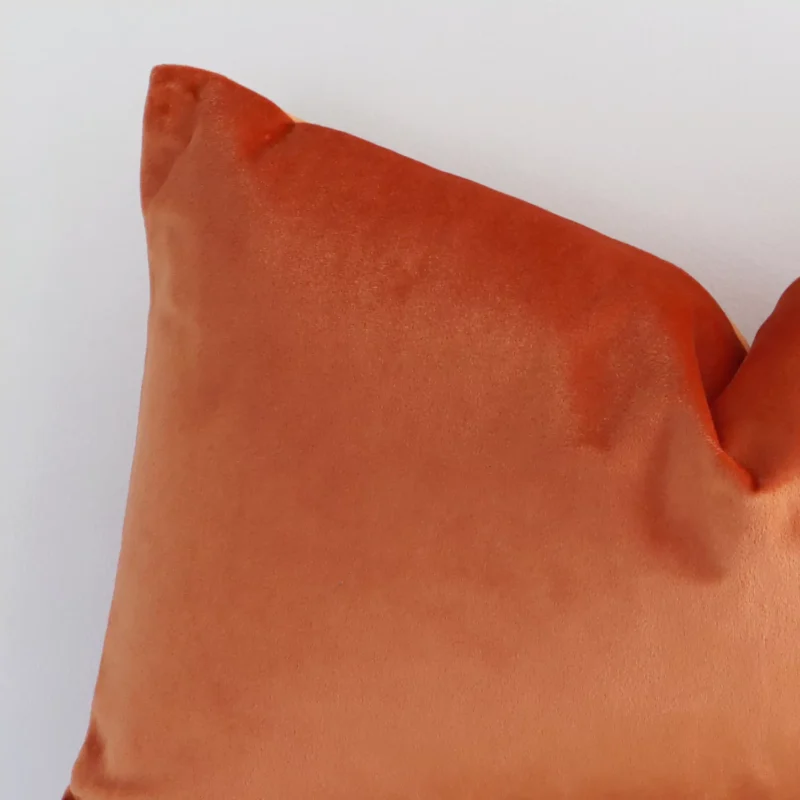 A zoomed in photo of the corner of a burnt solid-coloured cushion that has velvet fabric and a rectangle size.