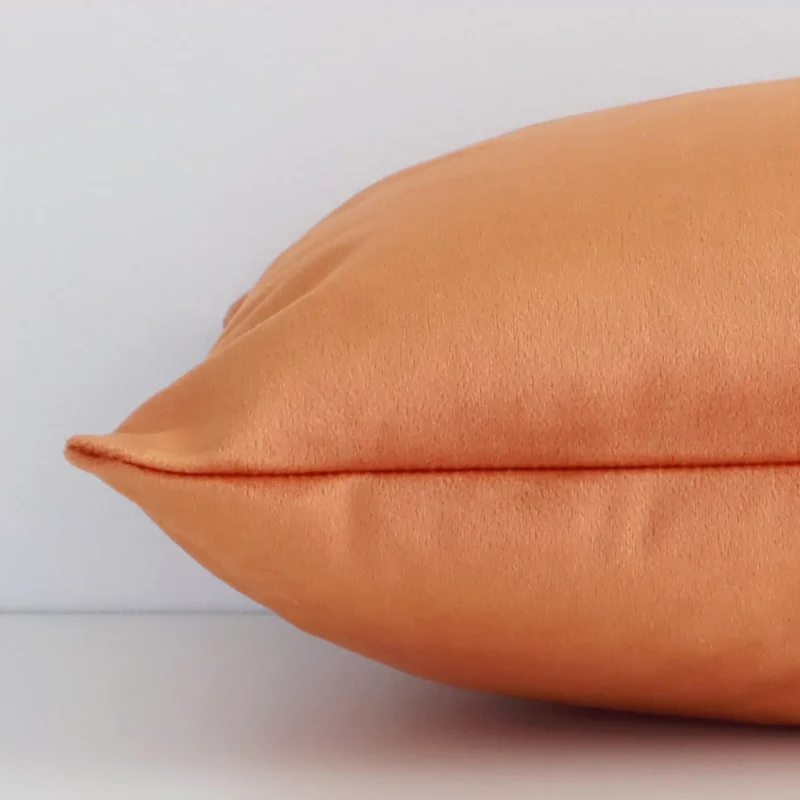 A rectangle velvet cushion positioned flat to show its seams. The burnt orange colour and solid colour design are visible as is the seam between the panels.
