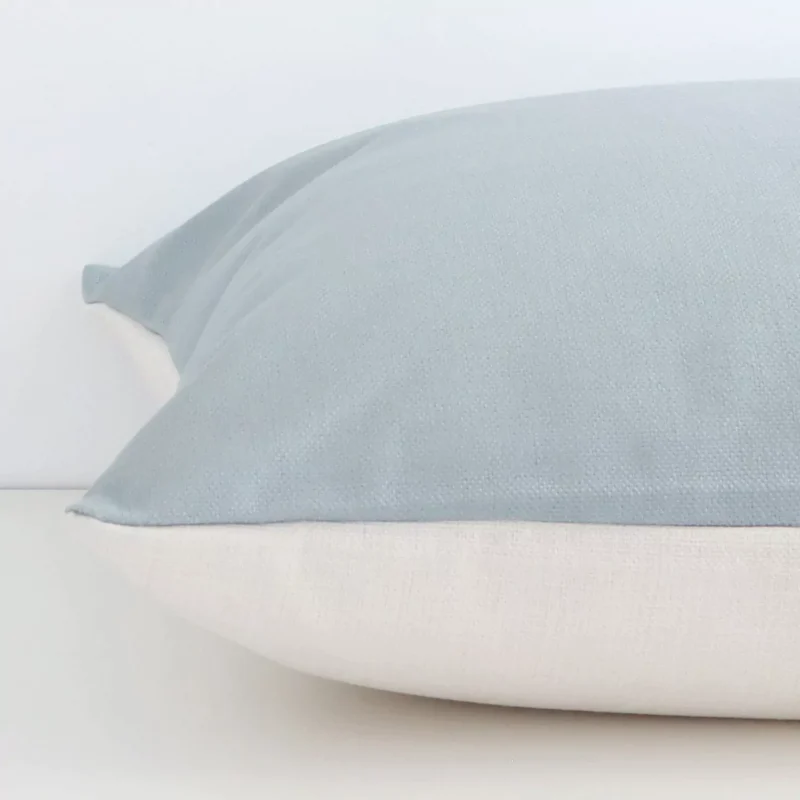 A solid-coloured soft teal cushion cover is laid flat. This angle shows the side of the linen fabric and its large size.