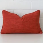 Here a burnt orange linen cushion is shown styled against a white wall. It has a rectangle design.