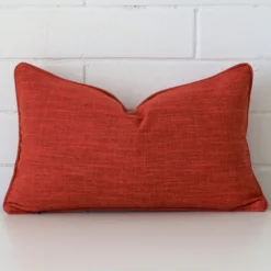 Here a burnt orange linen cushion is shown styled against a white wall. It has a rectangle design.