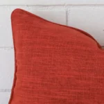 A very close image of the corner of a linen cushion.The finer detail of the rectangle shape and burnt orange colour are visible.