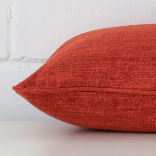 A side shot of a linen cushion cover. The angle shows the edge of the rectangle shape and the burnt orange tone.