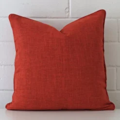 A pretty linen cushion cover is shown against a brick wall. It features a square shape and a burnt orange colour finish.