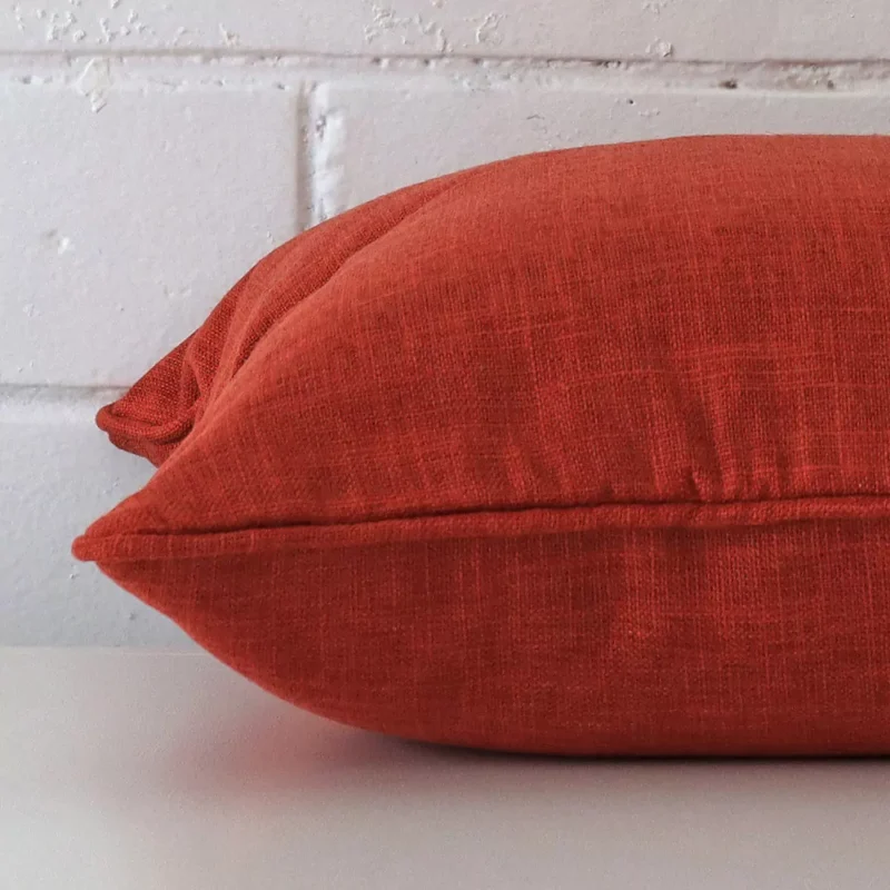 Lateral angle image of a linen square cushion. The burnt orange colour is highlighted.