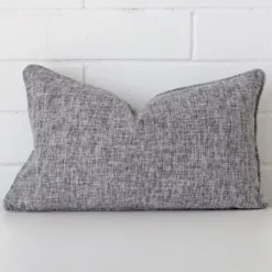 A linen rectangle cushion cover that is shown vertically against a brick wall. It has a wonderful grey colour.