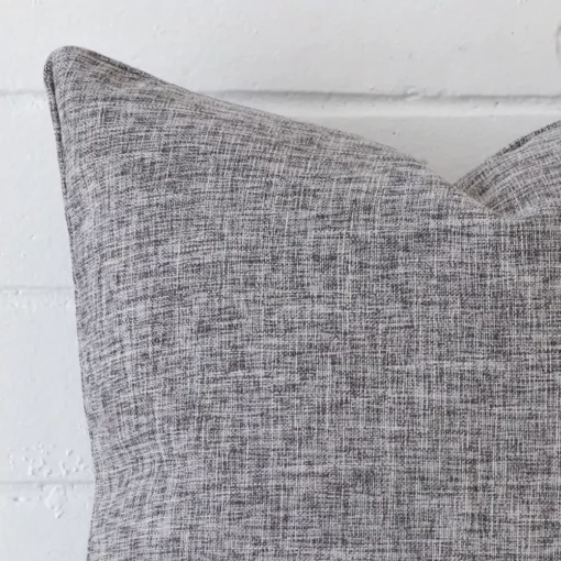 A very close image of the corner of a linen cushion.The finer detail of the square shape and grey colour are visible.