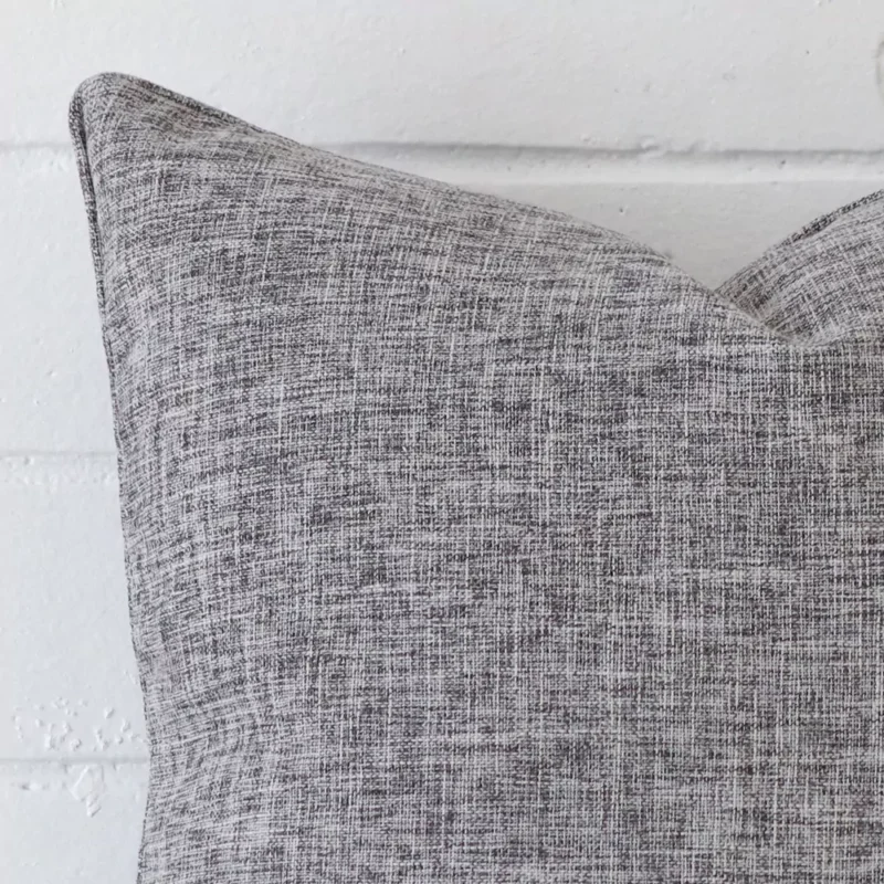 A very close image of the corner of a linen cushion.The finer detail of the square shape and grey colour are visible.