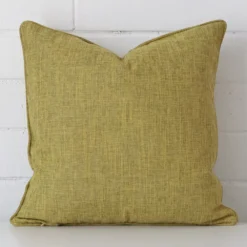 Olive cushion positioned in front of a brick wall. It has square dimensions and is made from a linen material.
