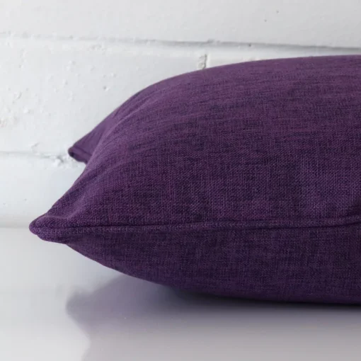 Purple cushion cover laid on its back side. The image shows a side-on view of the linen material and its square dimensions.