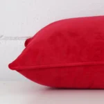 A side shot of a velvet cushion cover. The angle shows the edge of the rectangle shape and the red tone.