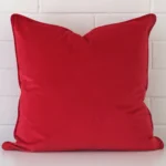 A brick wall that has a red cushion cover positioned in front of it. It has an exquisite velvet material and a lovely large size.