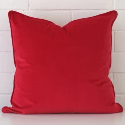 A brick wall that has a red cushion cover positioned in front of it. It has an exquisite velvet material and a lovely large size.