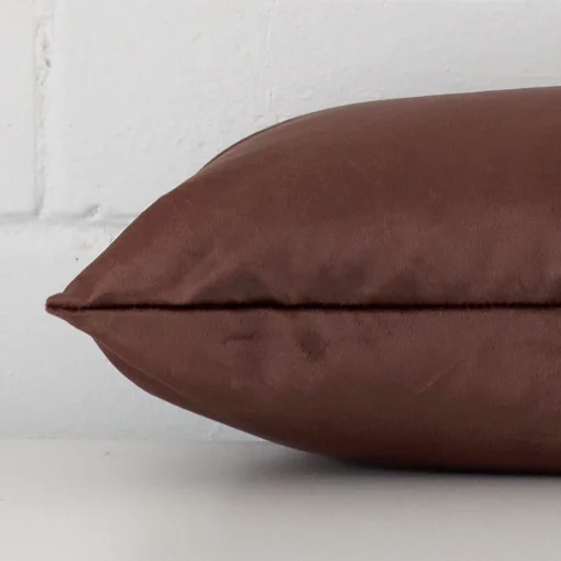 A square brown cushion cover laying flat. This viewpoint highlights the velvet fabric from a side position.