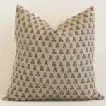 An attractive floral linen cushion in front of a white brick wall. It has a large shape and a sand colour.